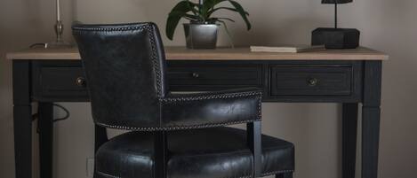 A desk with a leather chair, a potted plant, a map, a lamp, and a horse sculpture.
