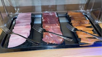 A buffet with various types of meat displayed in trays.