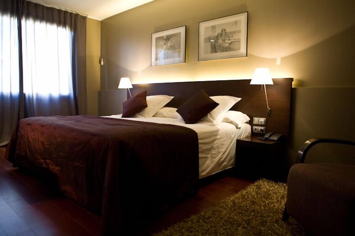 Een hotelkamer met een groot bed, twee bedlampen, een nachtkastje en twee ingelijste foto’s aan de muur.