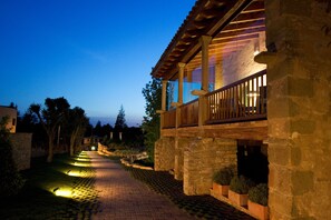 A stone building with a wooden balcony and a paved pathway. - Mas Albereda (Sant Julia de Vilatorta)