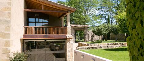 A two-story building with a balcony, stone walls, and a grassy courtyard.
