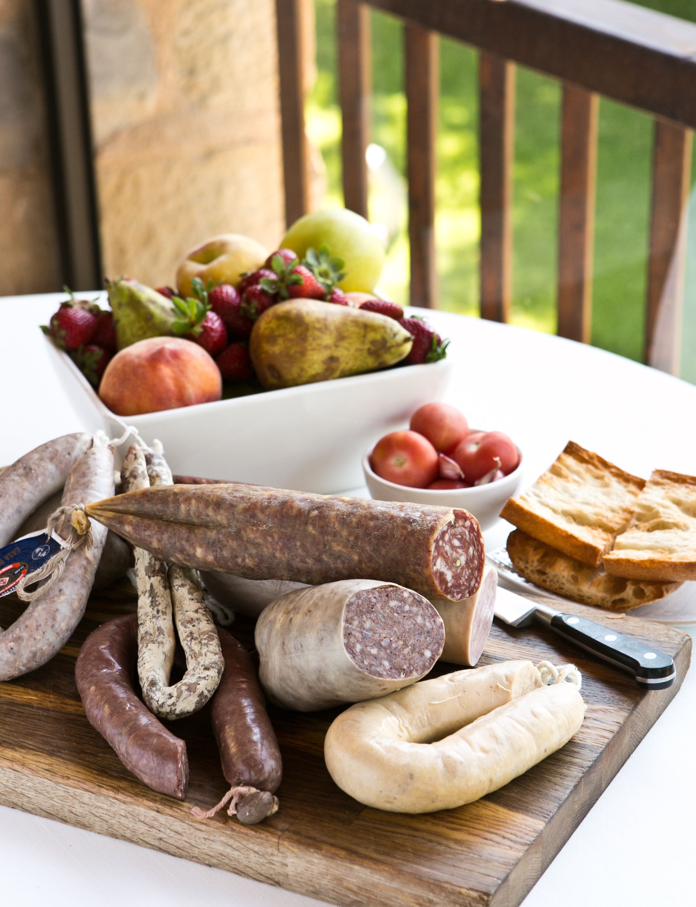 Una selección de embutidos curados y frutas frescas sobre una tabla de madera.