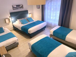 A hotel room with three beds, each with blue and white bedding, a wooden floor, and a large window with curtains. -   AUBERGE CAMILLE ET SIMON (Saint-Agnan)