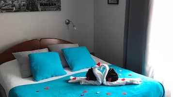 Un lit bien fait, avec une couverture bleue et des oreillers en forme de cœur, un tableau encadré au mur et une lampe.