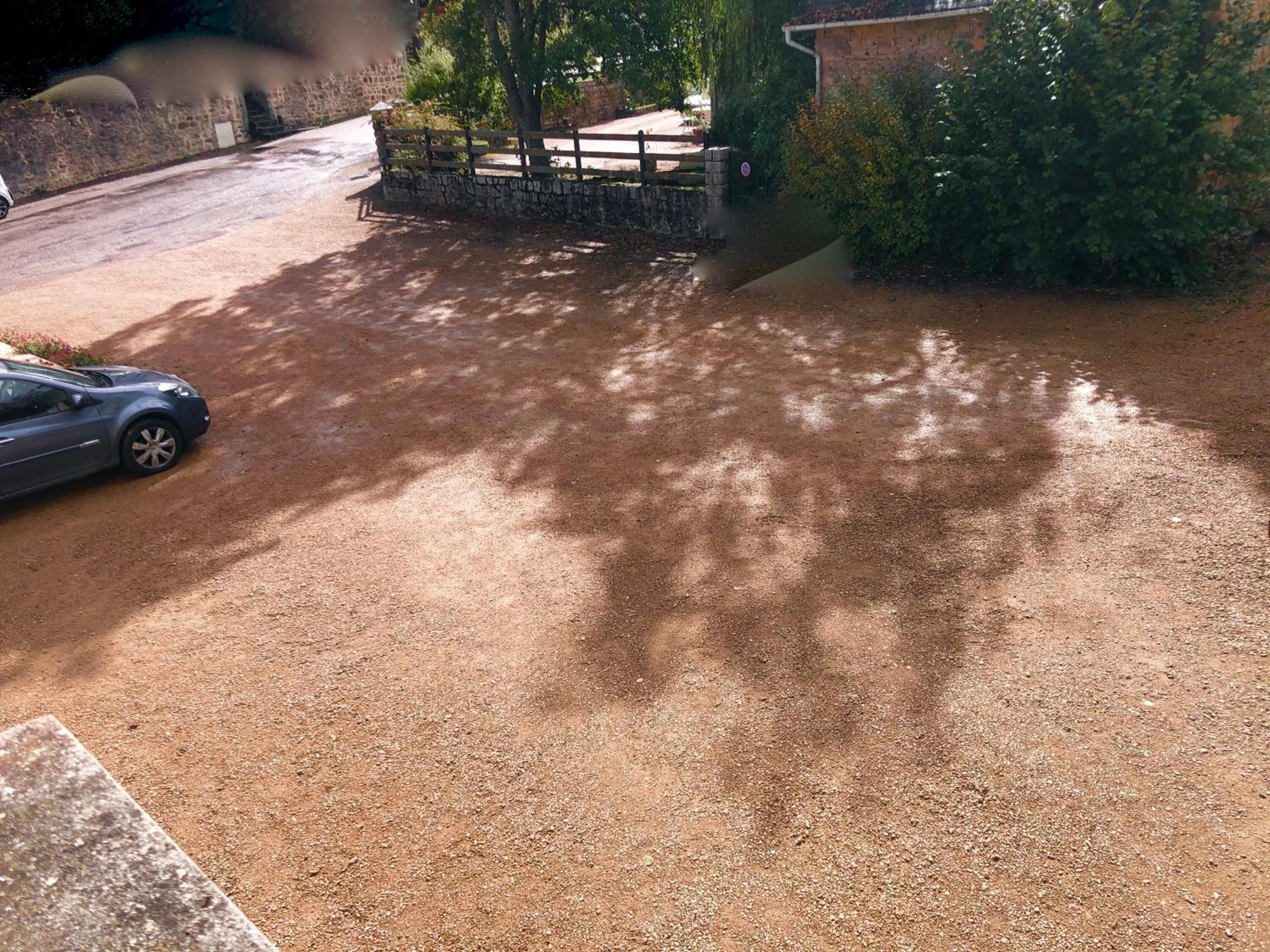 A gravel driveway leading to a stone wall and a wooden fence.