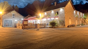 Un edificio de piedra con bar y restaurante en la planta baja, un área de estar al aire libre cubierta, y un estacionamiento al frente.