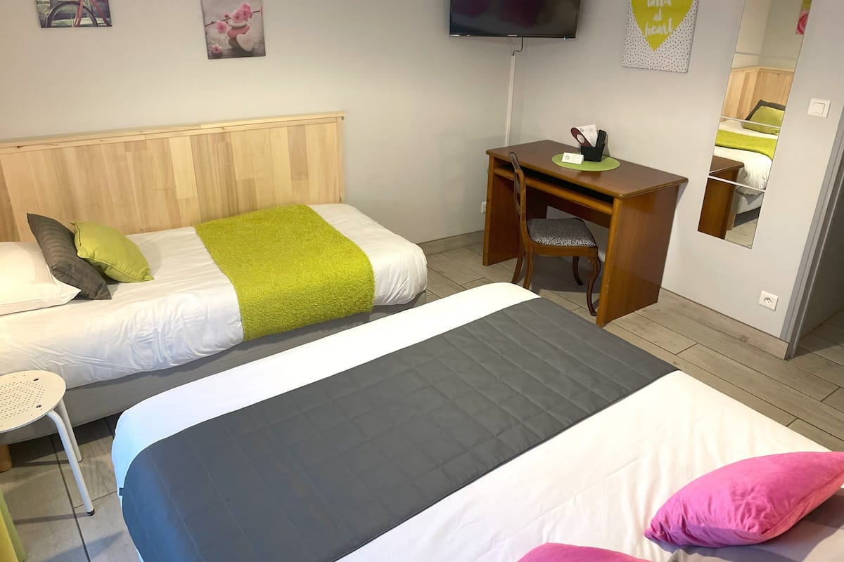 Habitación de hotel con dos camas, un escritorio, una silla, un televisor y obras de arte en las paredes.