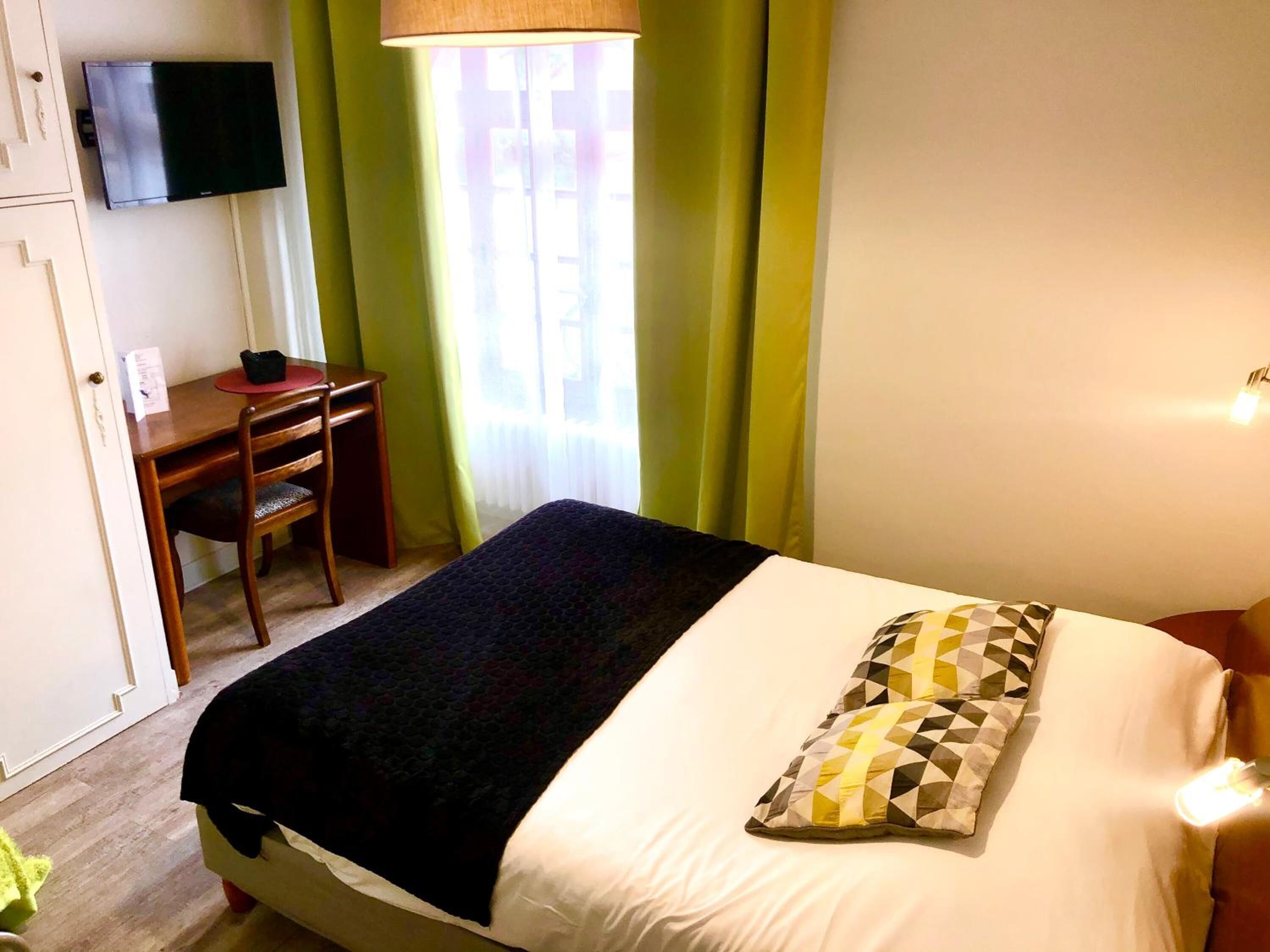 Een hotelkamer met een bed, een bureau, een stoel, een televisie aan de muur en een raam met gordijnen.