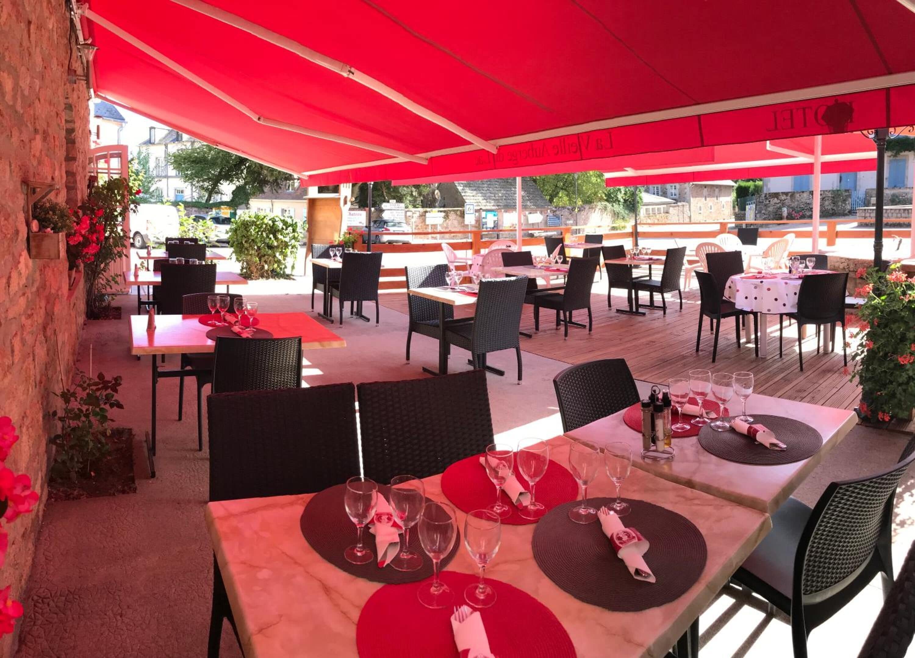 An outdoor dining area with red umbrellas, tables set with wine glasses and red napkins, and wicker chairs.