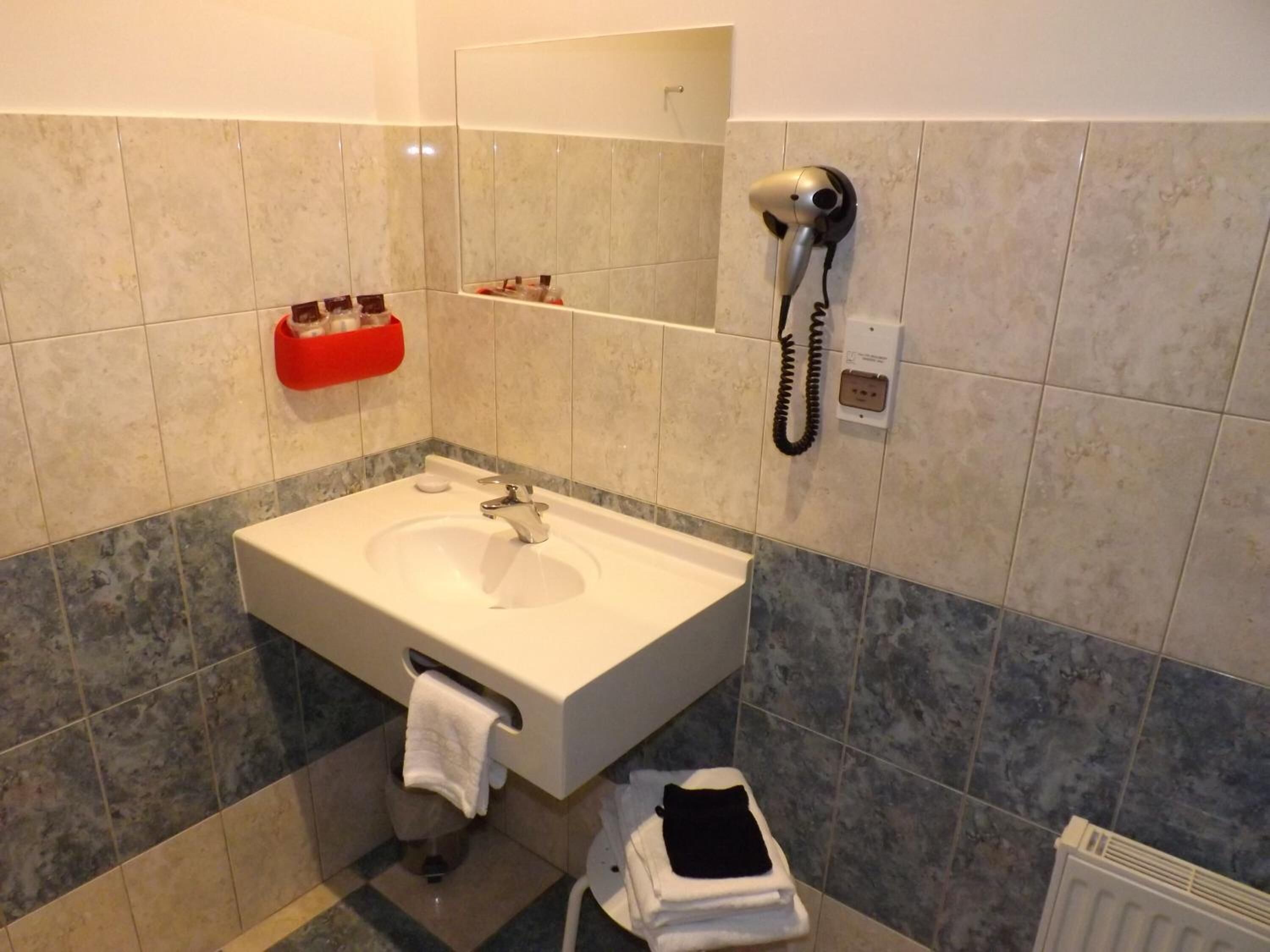 Un bagno con un lavandino bianco, un porta asciugamani, un asciugacapelli e un portasapone rosso.