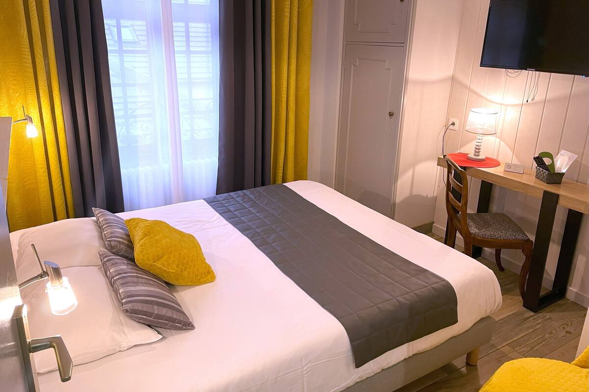 Habitación de hotel con cama, escritorio, silla, televisor y ventana con cortinas.