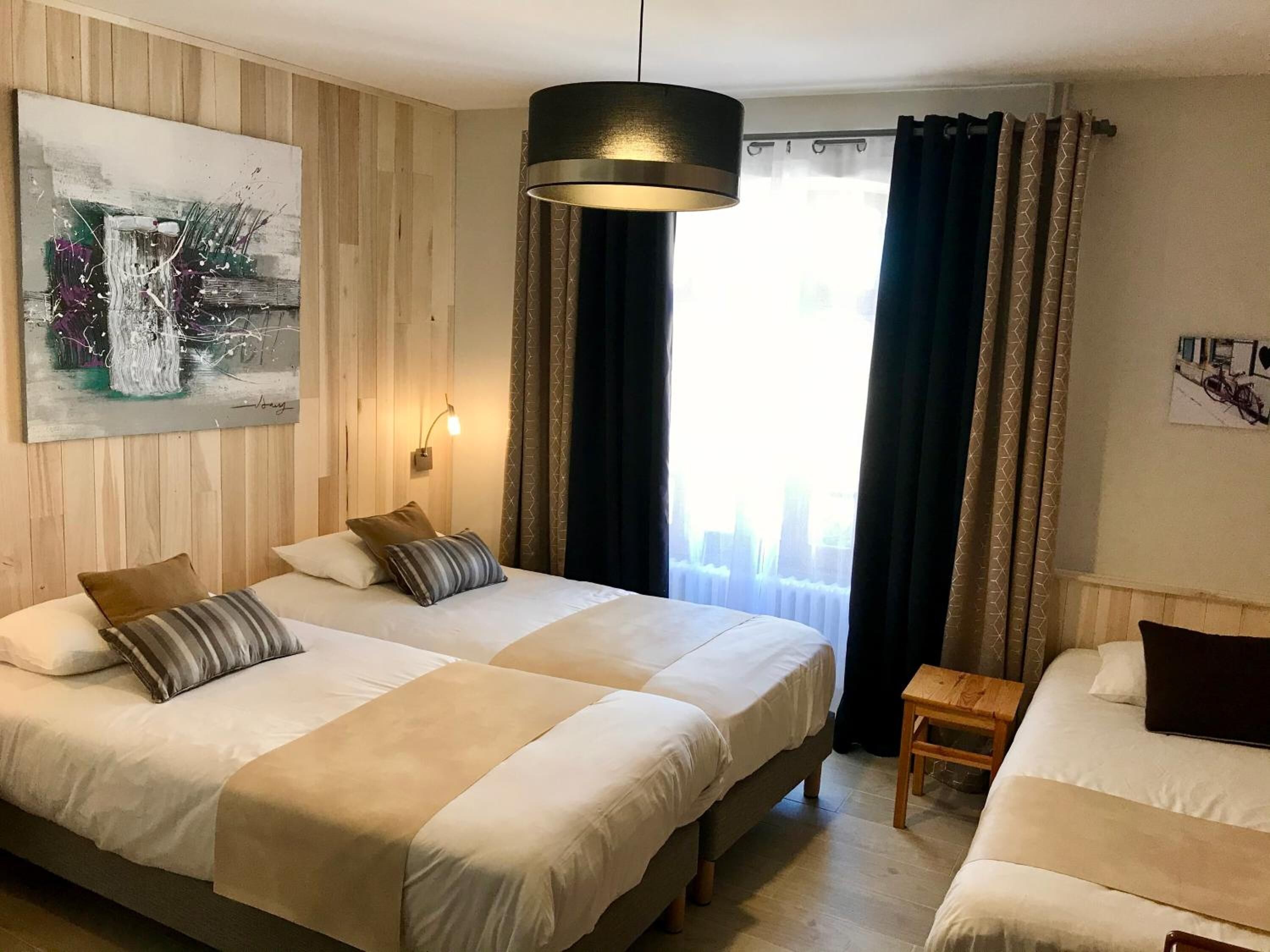 Quarto de hotel com duas camas, um quadro na parede, um lustre e uma janela com cortinas.