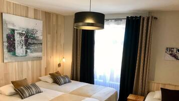Quarto de hotel com duas camas, um quadro na parede, um lustre e uma janela com cortinas.