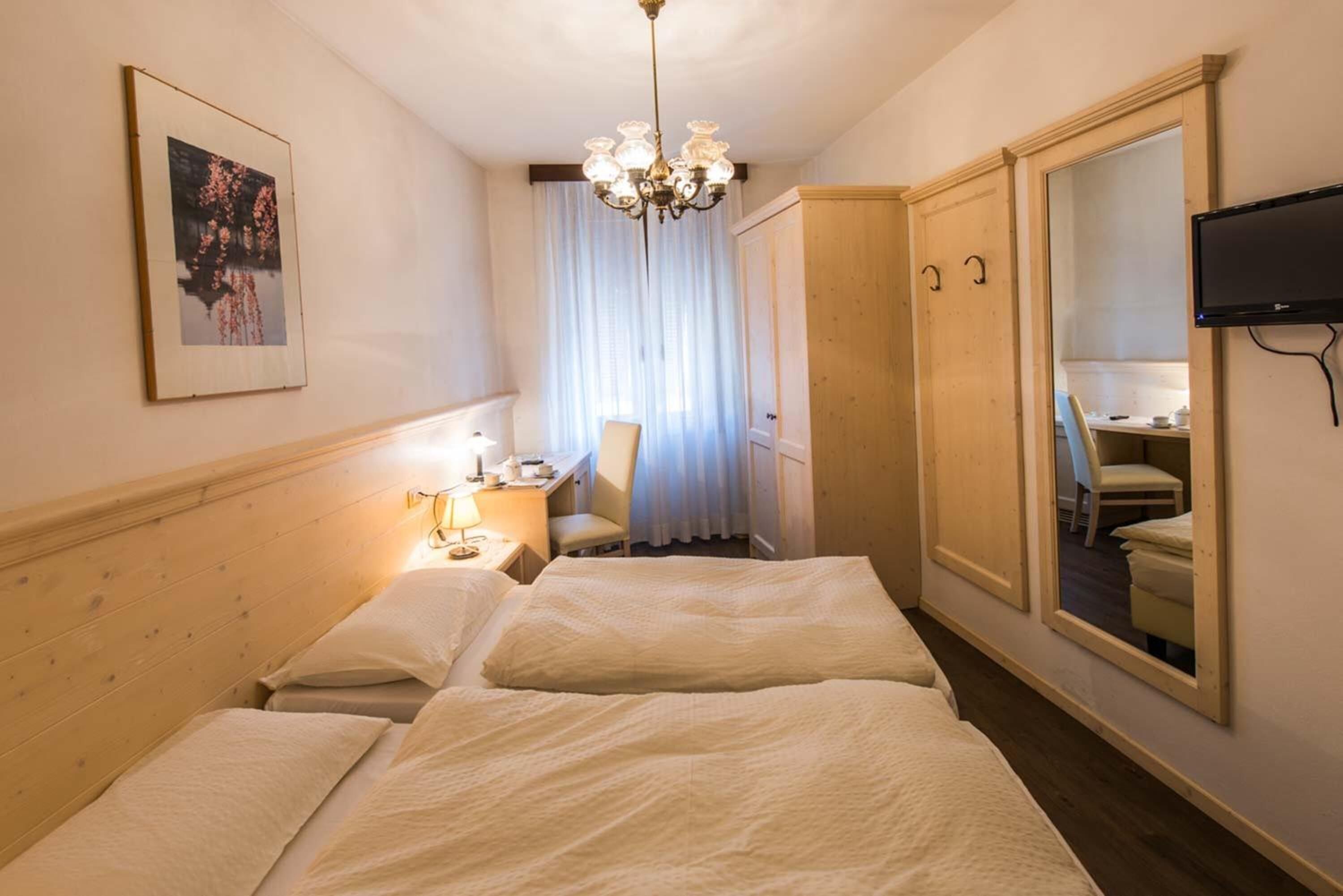 A hotel room with a bed, bedside table, lamp, chair, and a mirror.