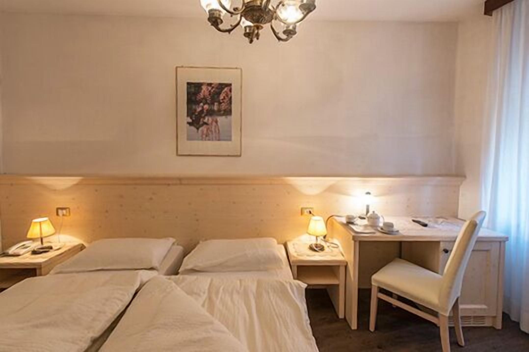 A hotel room with two beds, a desk, a chair, and a chandelier.