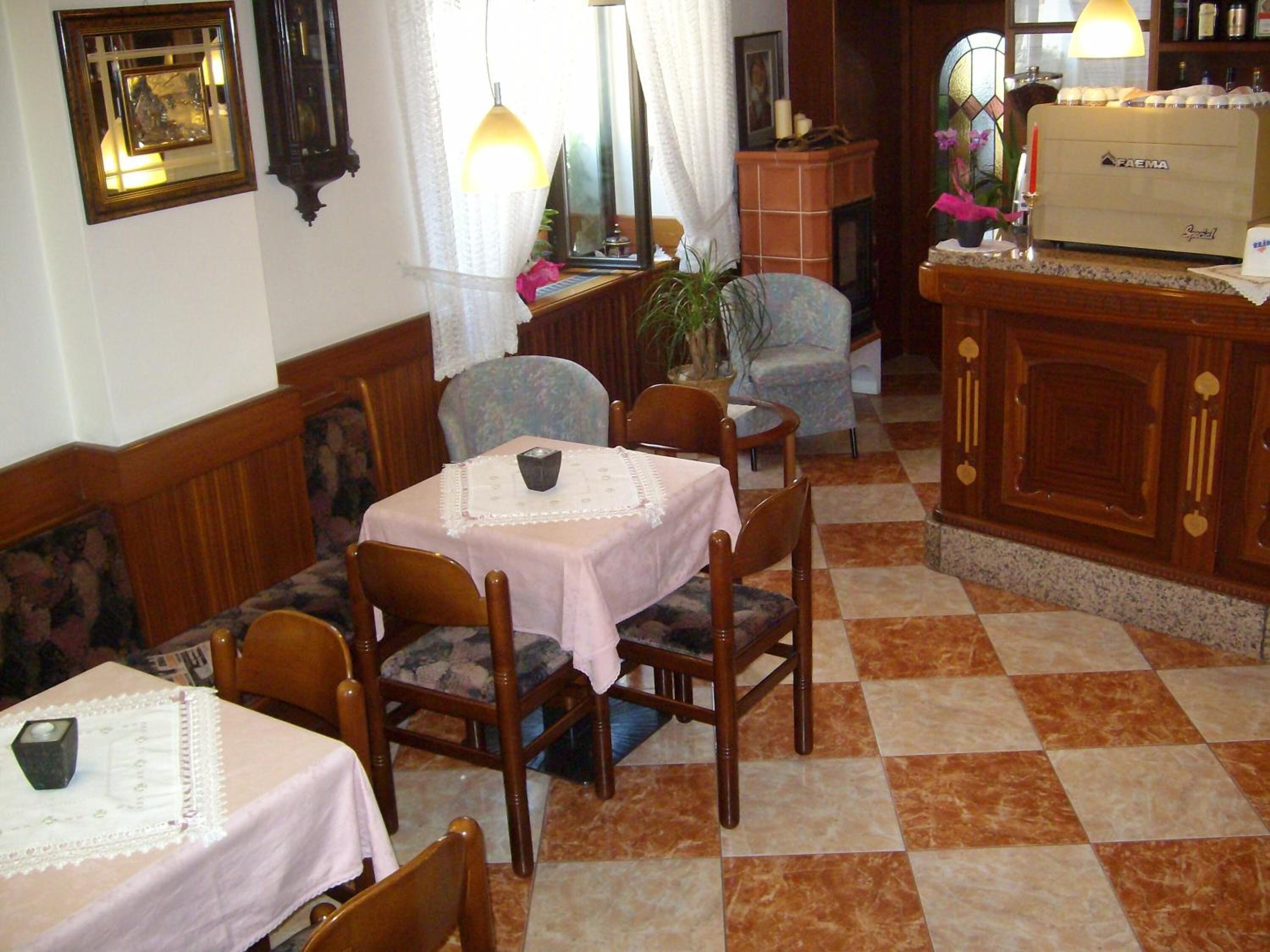 A dining area with wooden chairs and tables, a bar area with a Faema espresso machine, and a checkered floor.