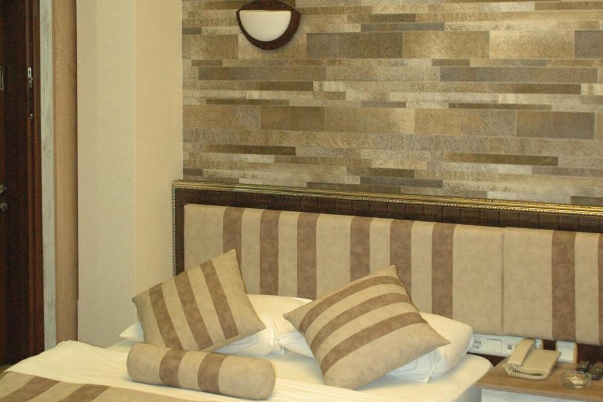 A hotel room with a bed, a nightstand, a telephone, and a wall with a textured pattern.