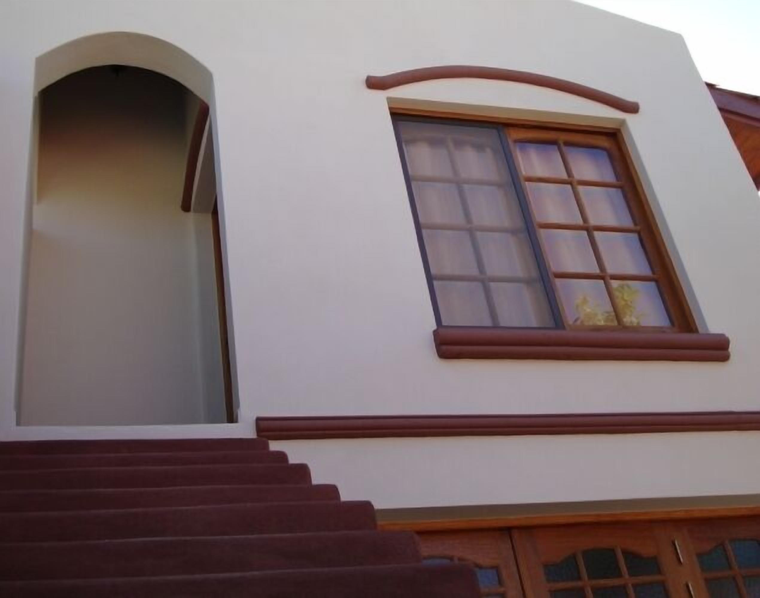 A building with a white facade, a large arched window, and a set of stairs leading to a door with glass panels.