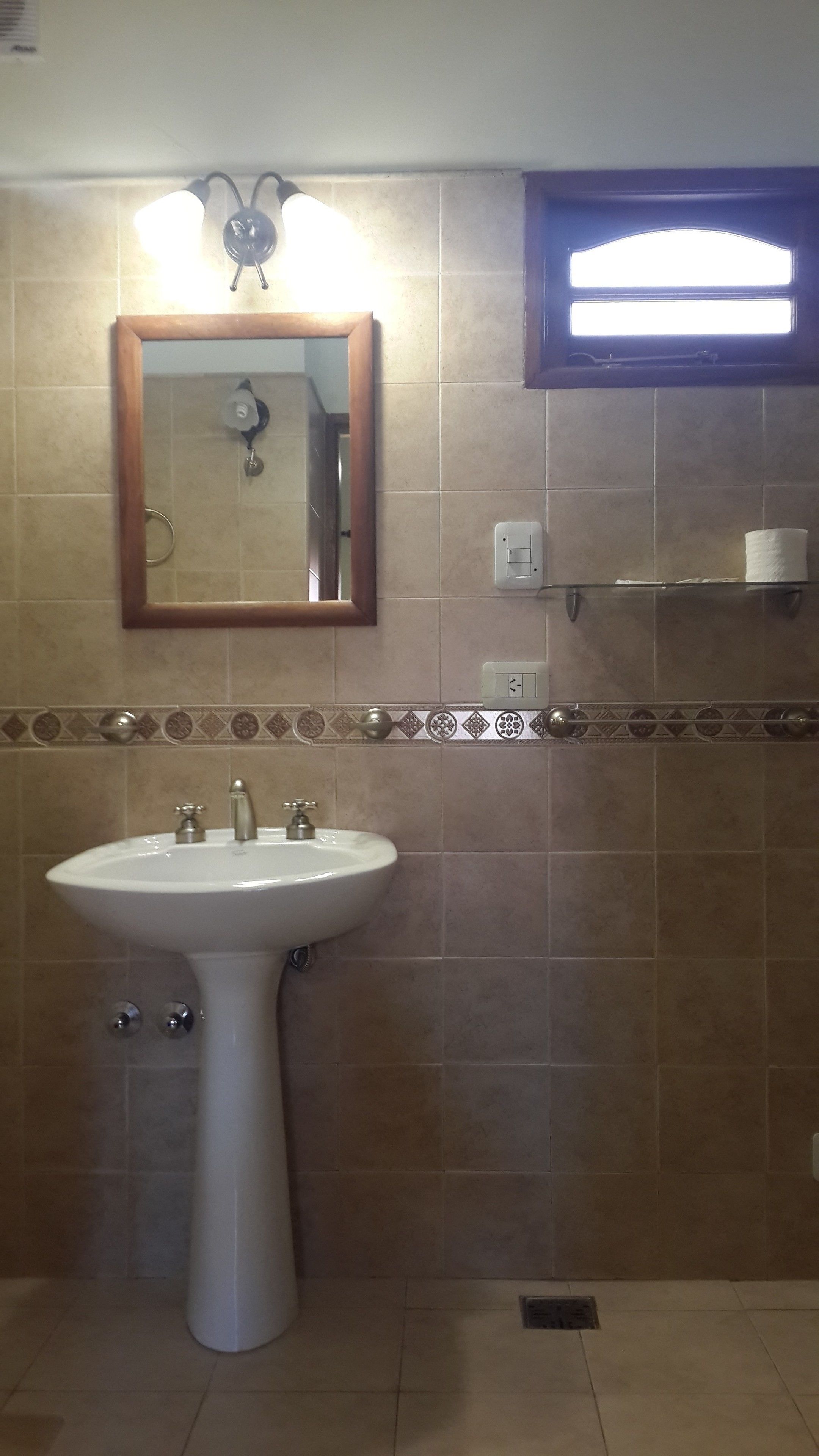 Un baño con lavamanos pedestal, un espejo, un perchero para toallas y un dispensador de papel higiénico.