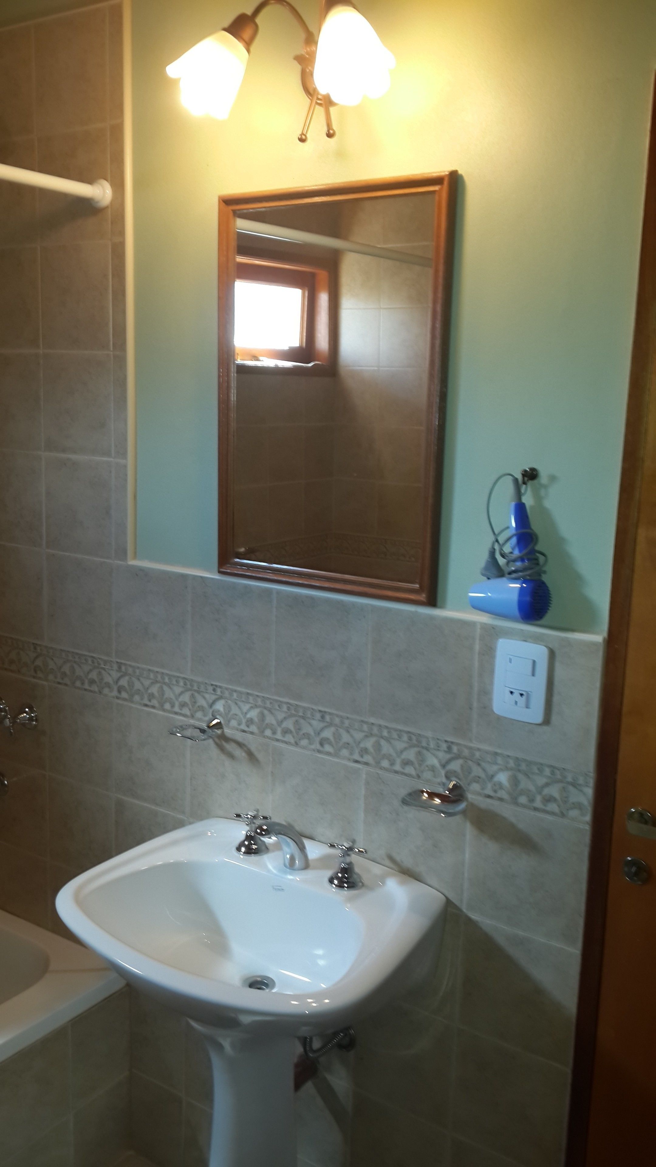 Un baño con un lavamanos blanco, dos grifos, un espejo y un perchero para toallas.