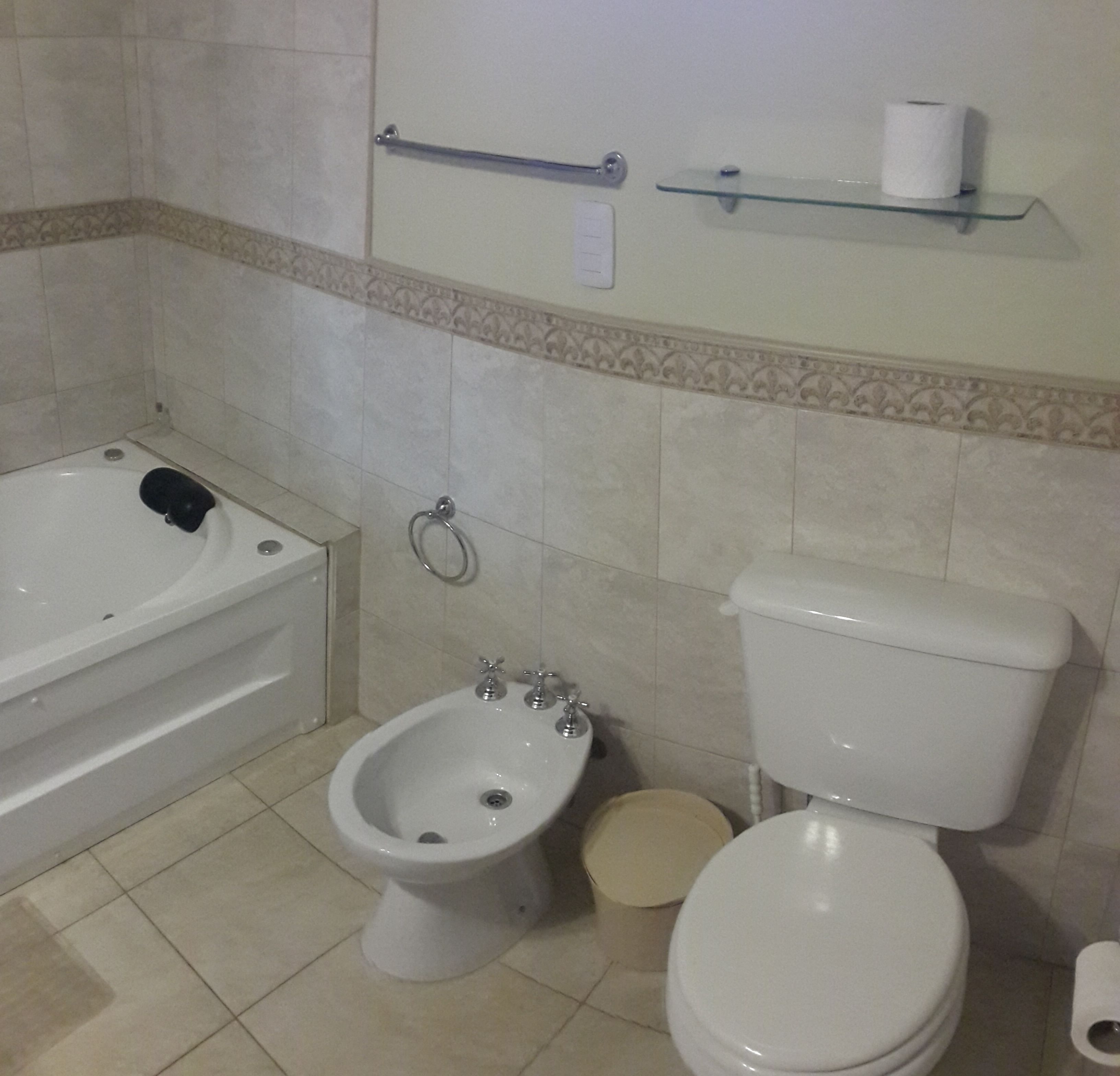 Un baño con bañera, bidé, inodoro y un estante con un rollo de papel higiénico.