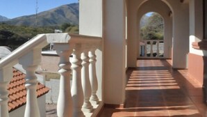 Un pasillo con balaustradas blancas, suelo de baldosas y vista a montañas distantes.