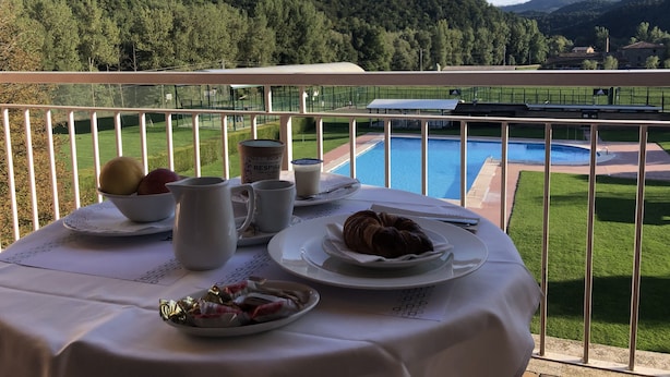 A table set with breakfast items on a balcony overlooking a pool and a mountainous landscape. - Hotel Solana del Ter (Ripoll)
