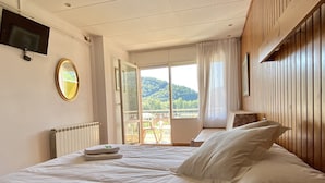 A hotel room with a large bed, a TV mounted on the wall, a mirror, and a view of a balcony with a scenic landscape. - Hotel Solana del Ter (Ripoll)