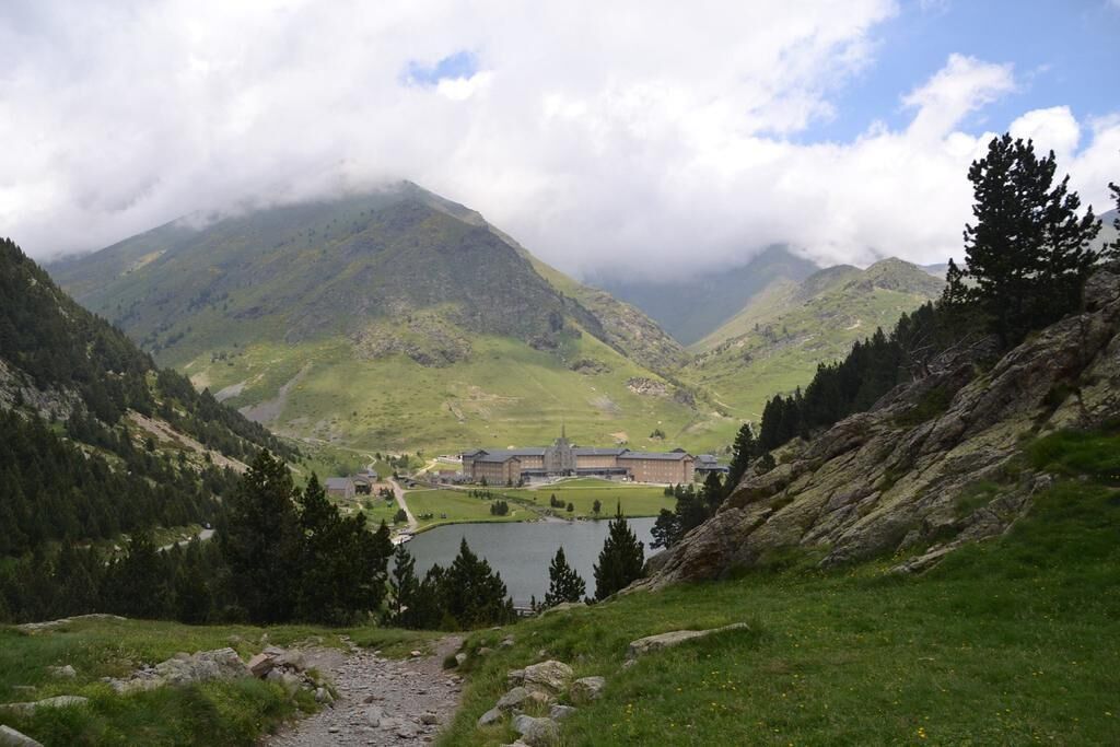 A mountain landscape with a building featuring a large central courtyard and a lake in the foreground.