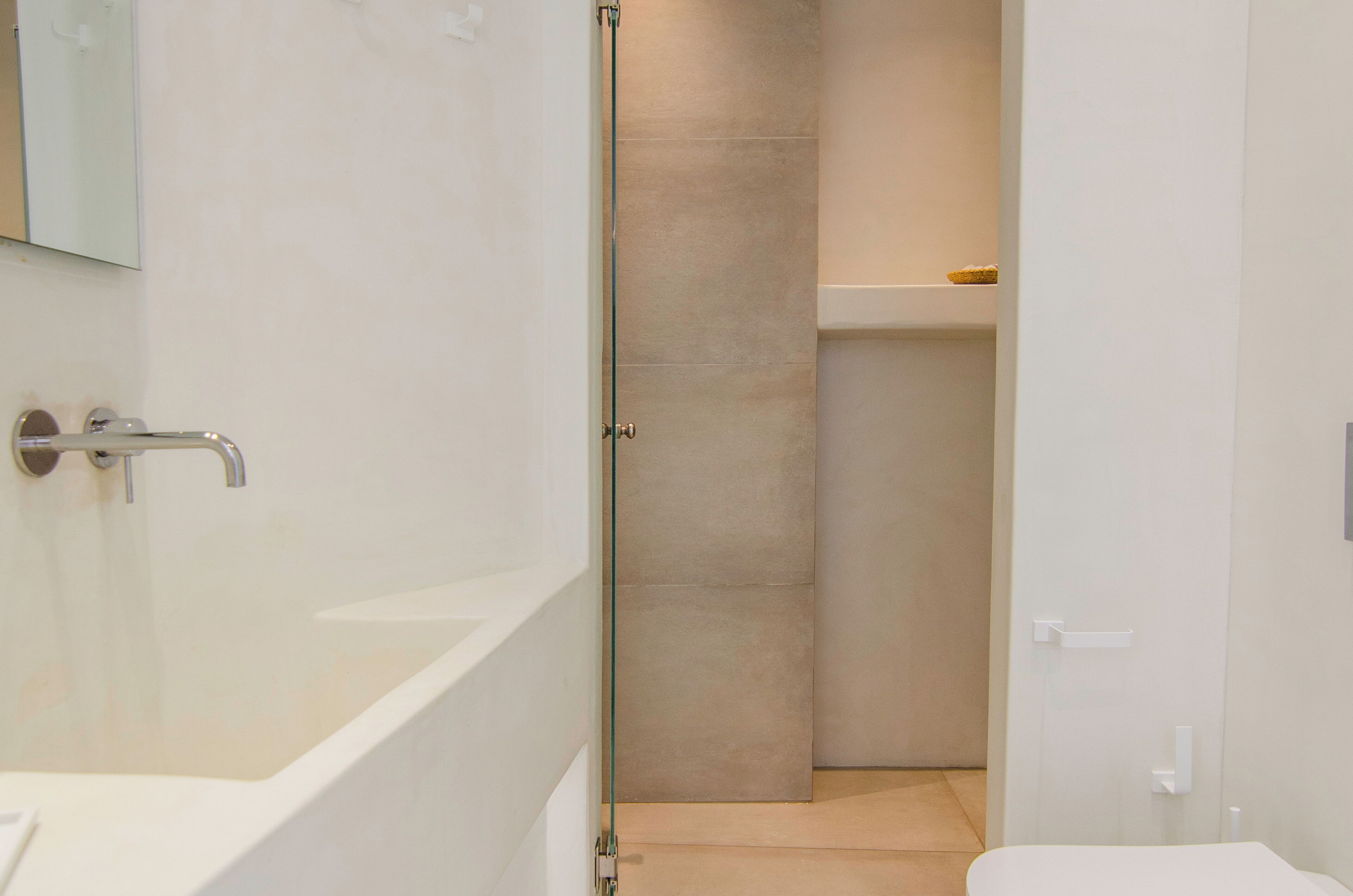 A modern bathroom with a glass-enclosed shower, a white bathtub, and a small shelf with a towel.