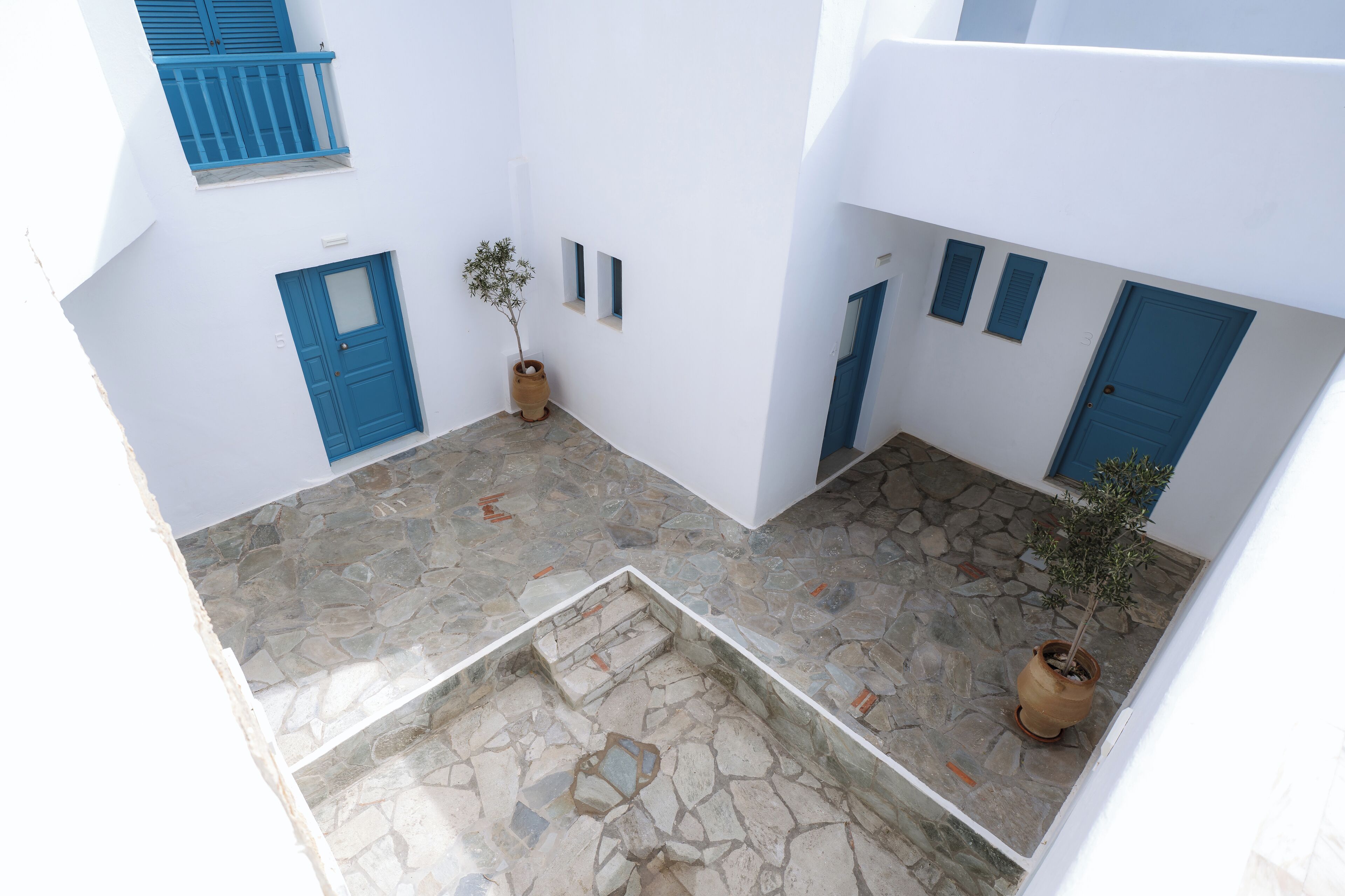 A courtyard with stone flooring, white walls, and blue doors and shutters.