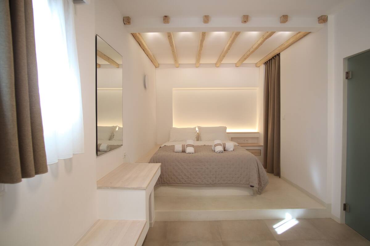 Een moderne slaapkamer met een groot bed, nachtkastjes, een spiegel en een houten plafond.