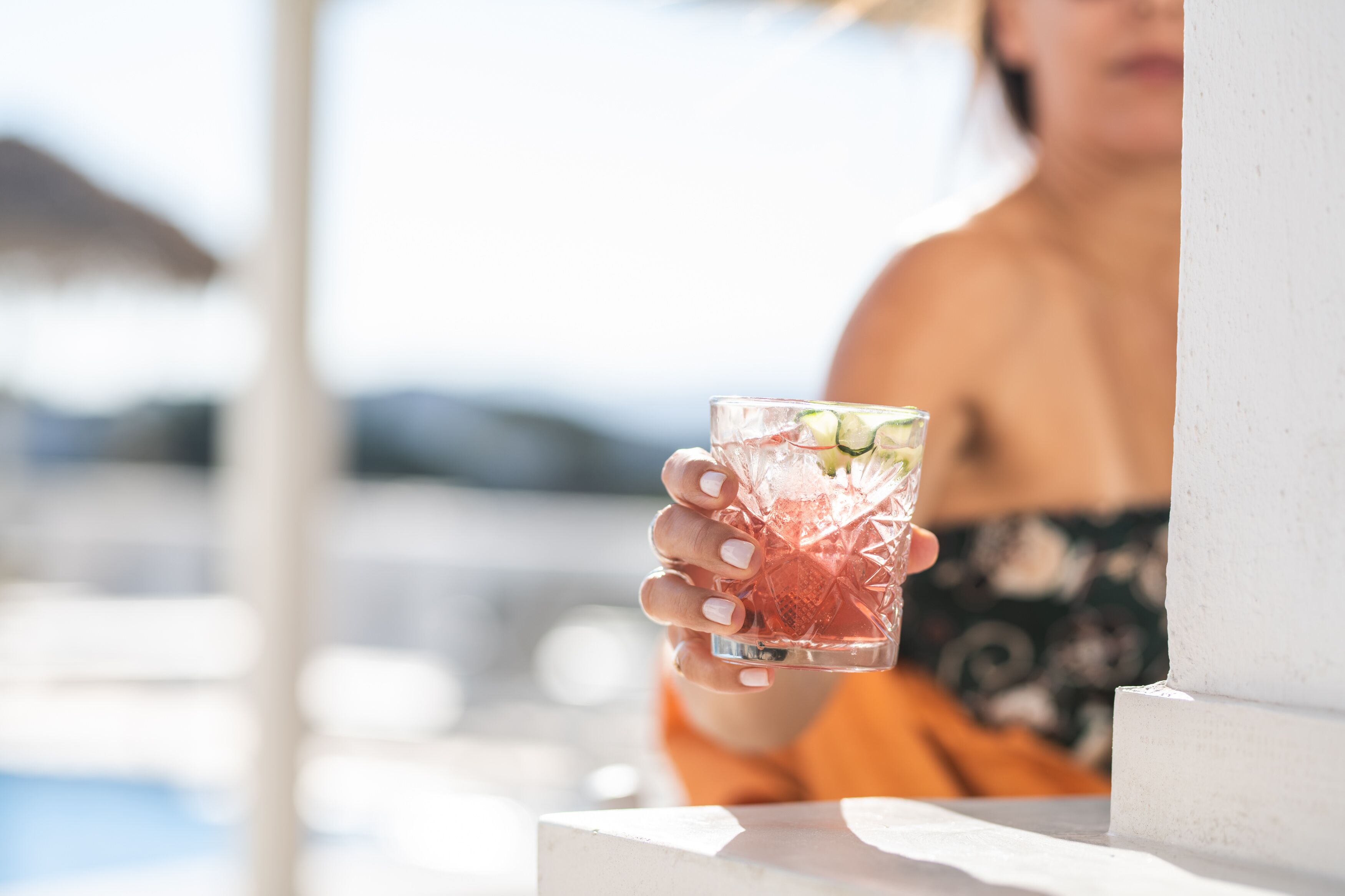 A person holding a cocktail glass with a tropical drink, near a poolside area.
