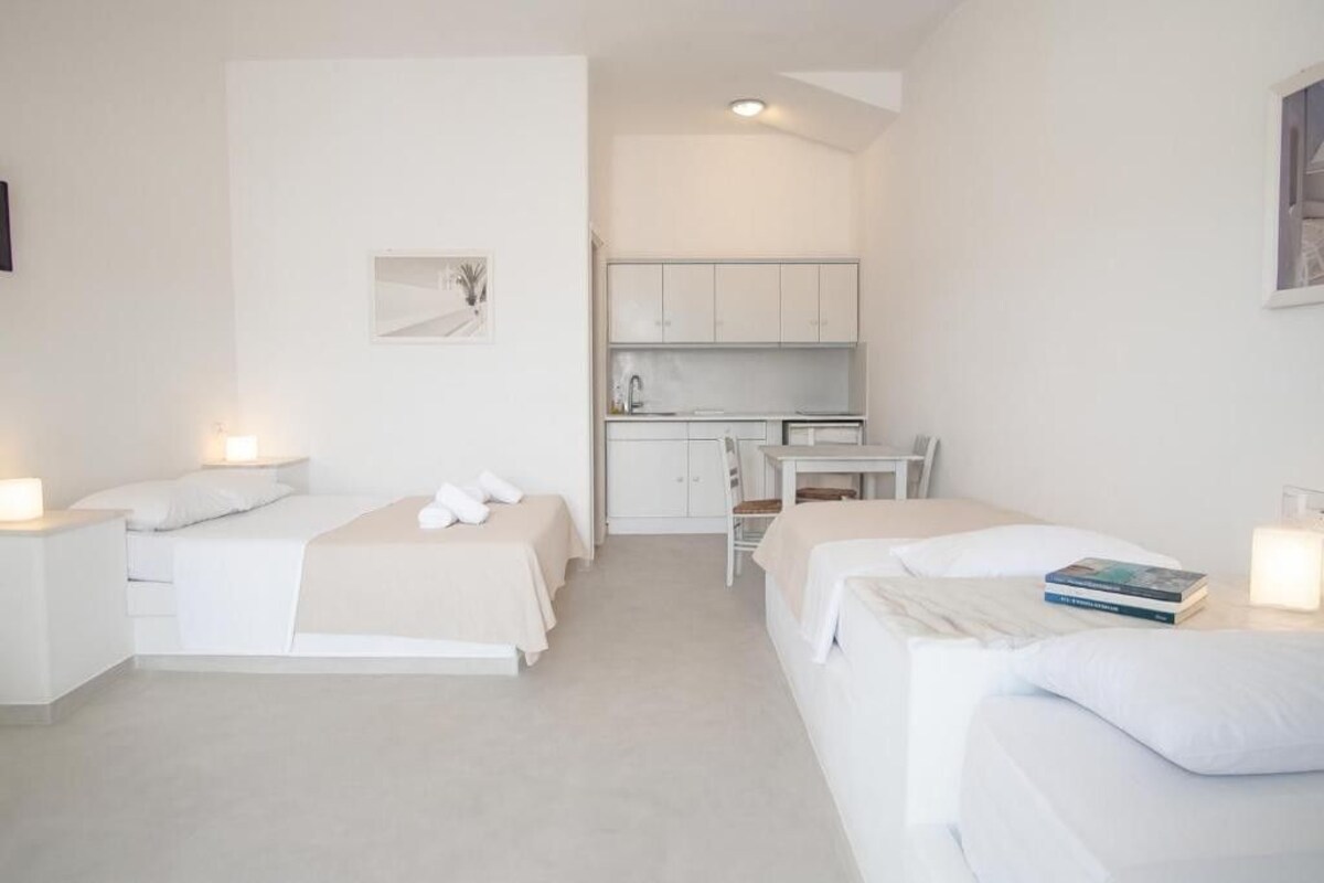 A compact hotel room with two single beds, a small kitchenette, and a desk.