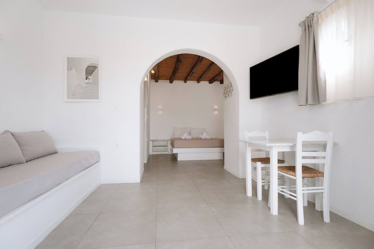 Een moderne, minimalistisch ingerichte slaapkamer met een bed, een bank, een televisie en een zithoek.