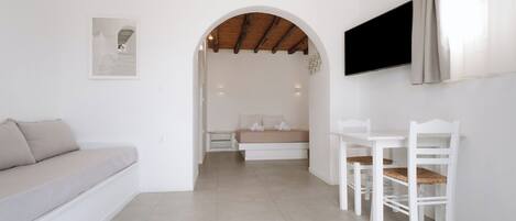 A modern, minimalist bedroom with a bed, a sofa, a TV, and a dining area.