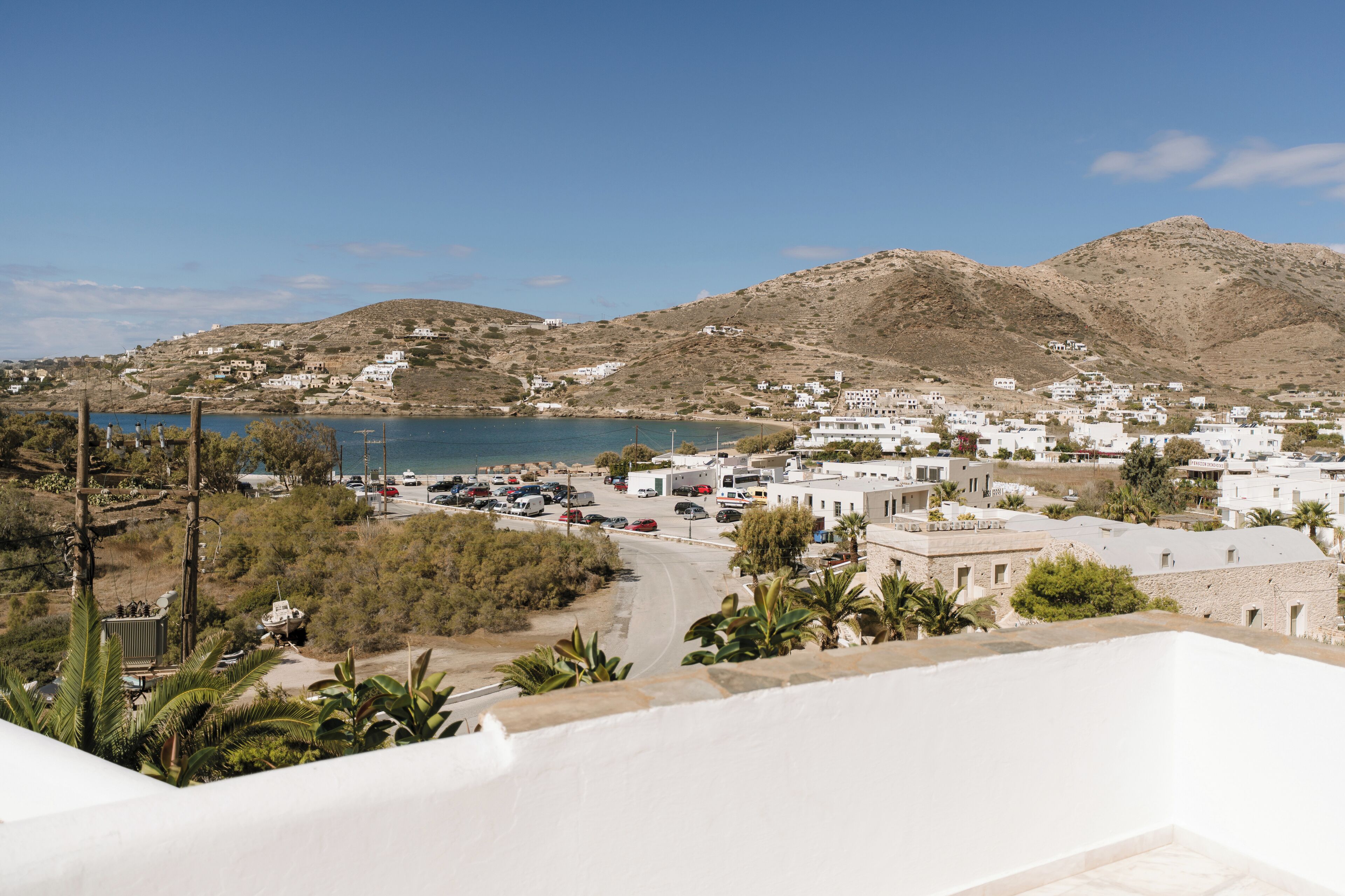 A coastal town with white buildings, a parking area, and a view of the sea and hills.