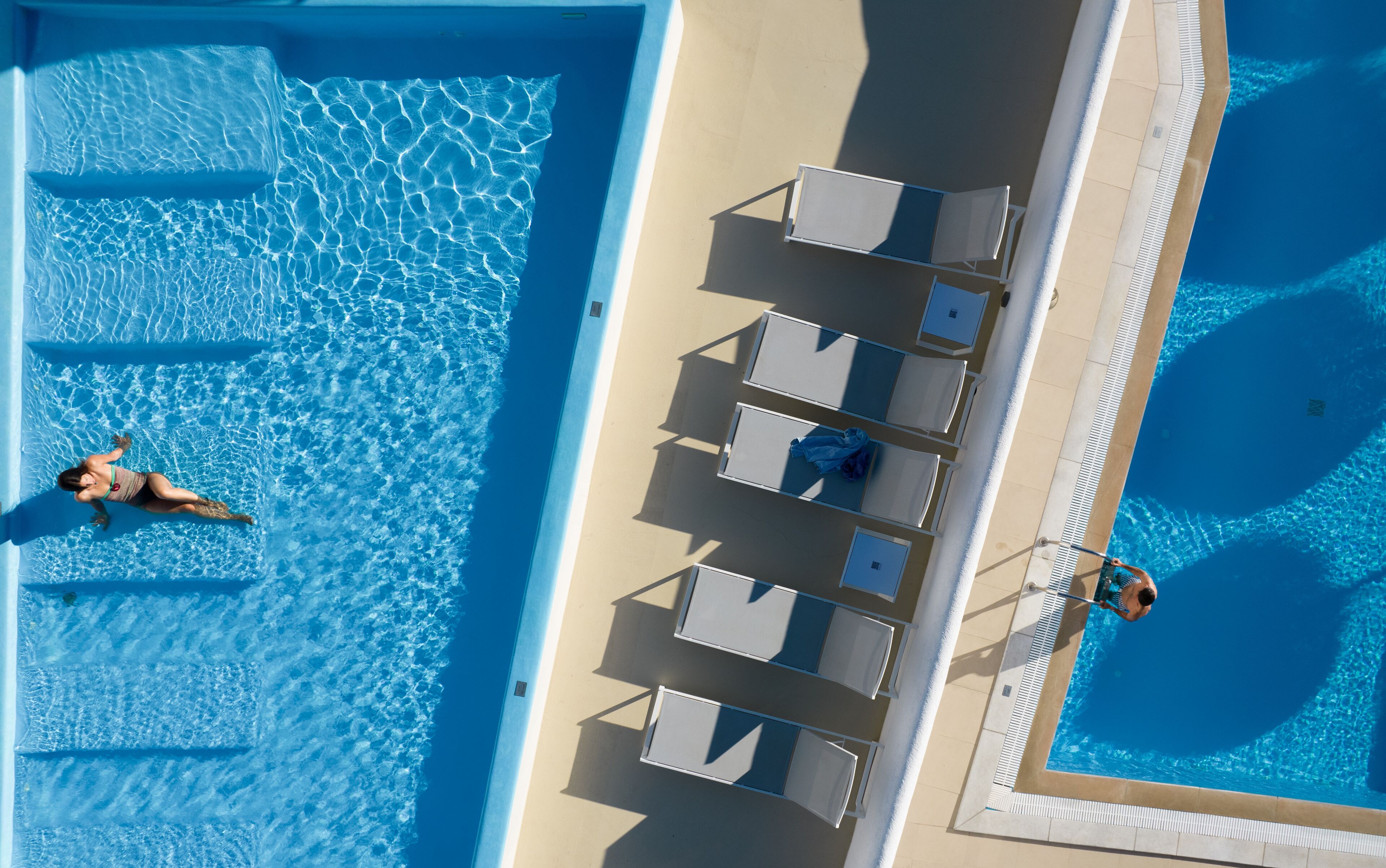 Vista aérea de una piscina con sillas de descanso y una persona nadando.