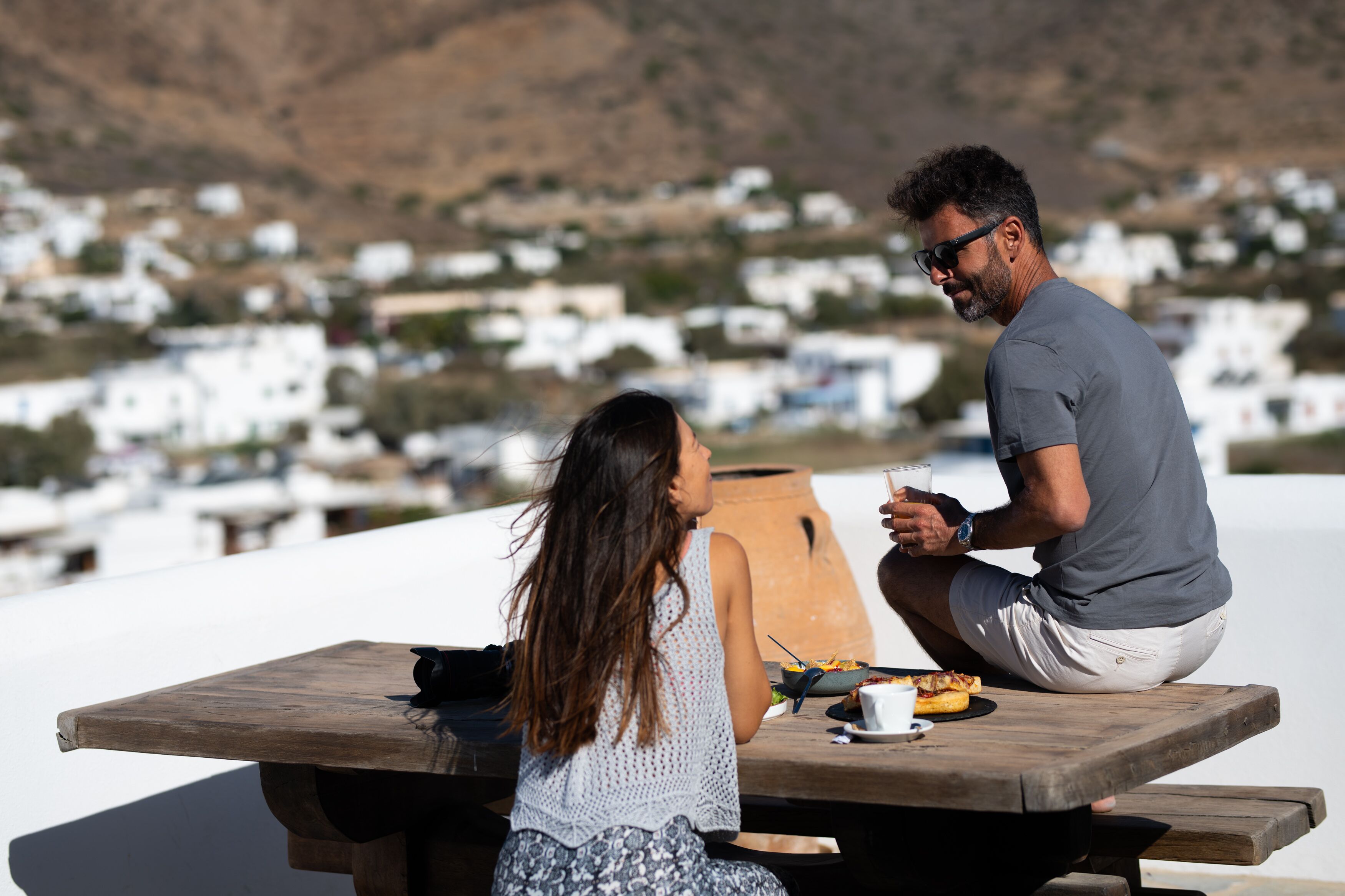 A couple dining at a wooden table with a view of white buildings in the background.