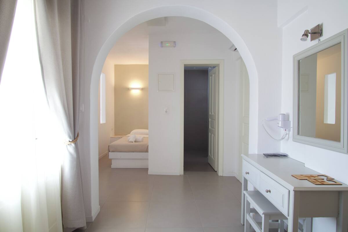 Een hotelkamer met een witte kaptafel, een spiegel en een bed met witte lakens.