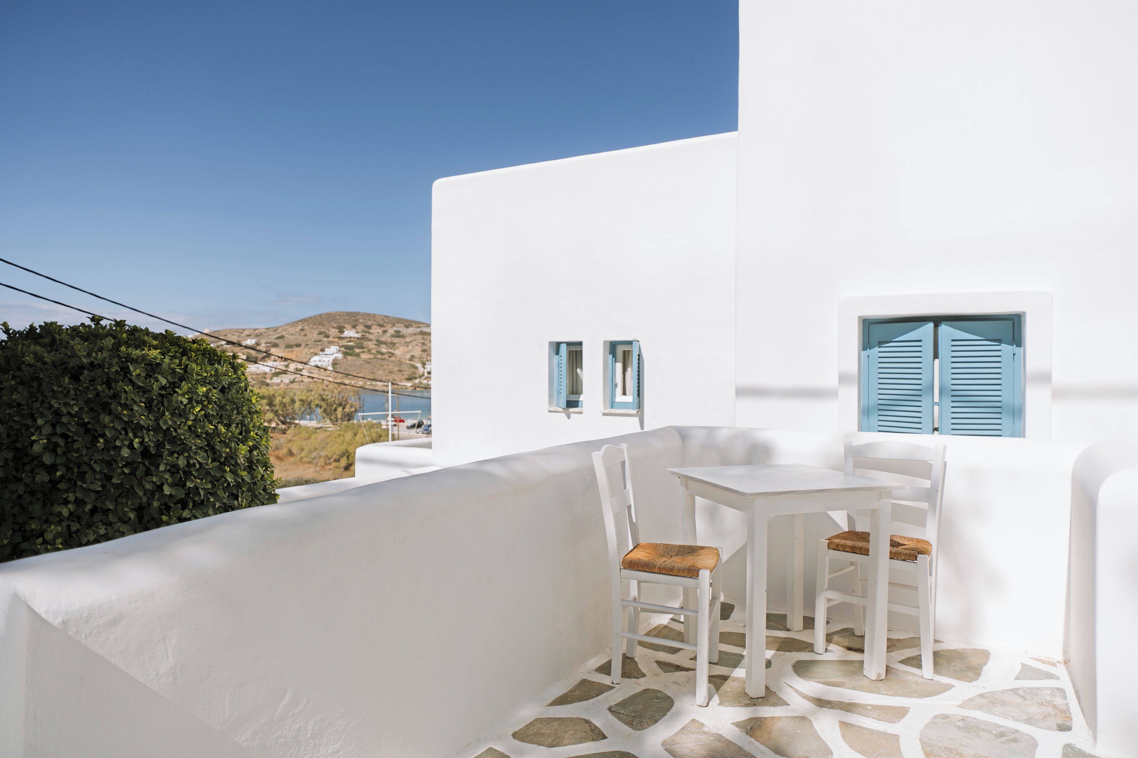 Un edificio blanco con suelo de piedra, una mesa con dos sillas y vistas a una colina.
