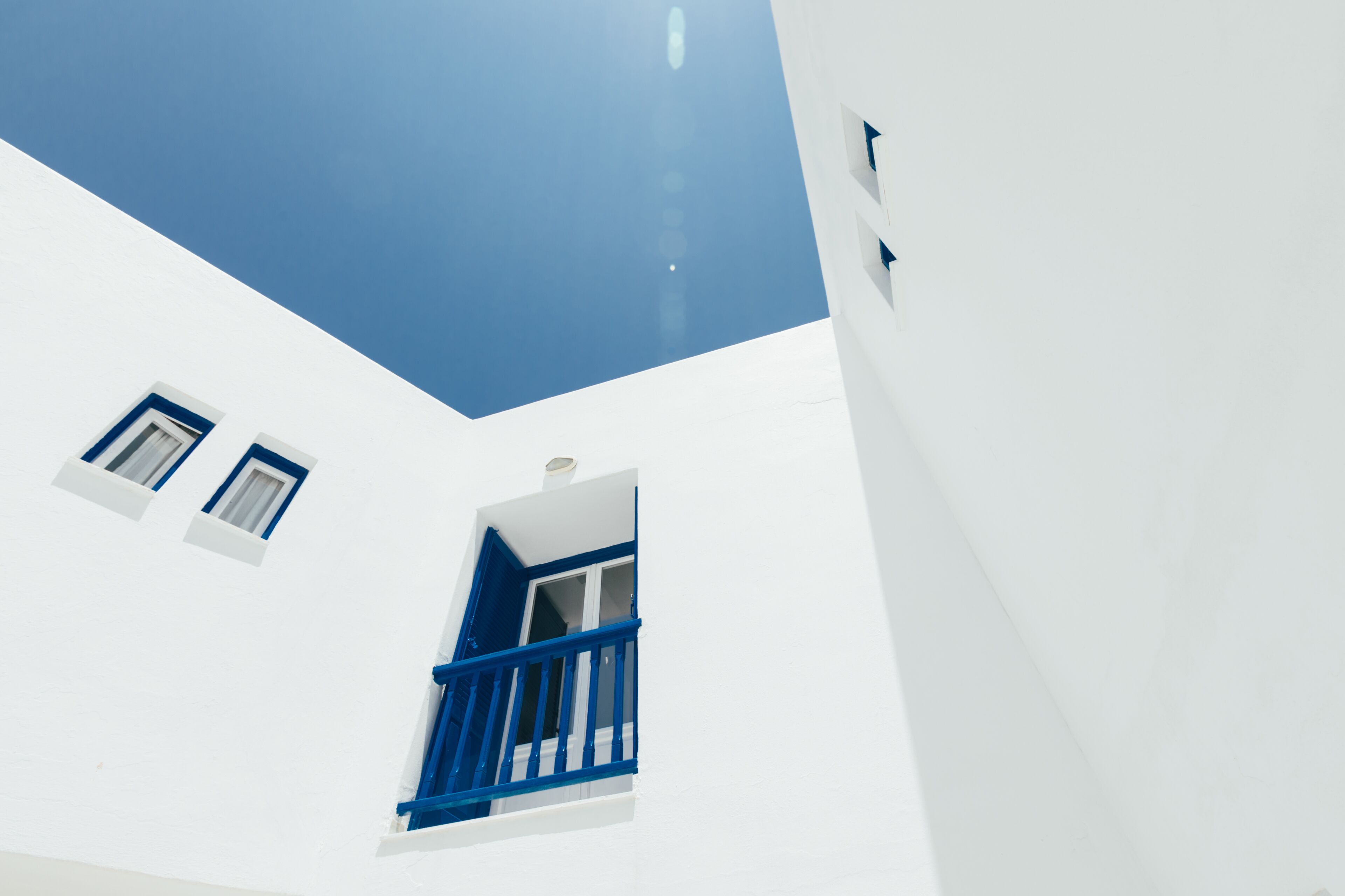 A white building with blue accents, including a window with a blue frame and a balcony.