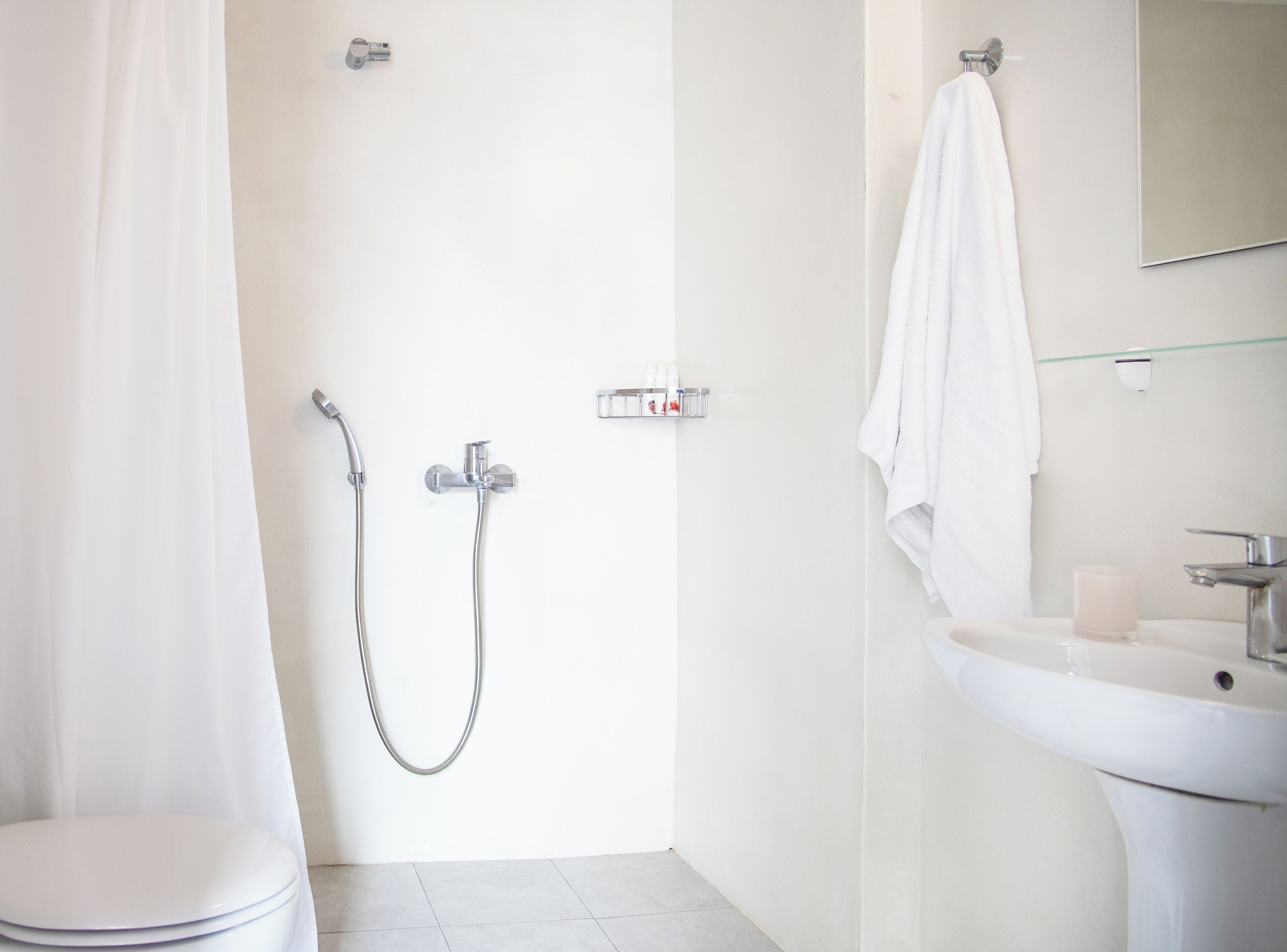 A bathroom with a toilet, a shower with a handheld showerhead, a glass shower enclosure, a sink with a mirror, and a towel hanging on the wall.