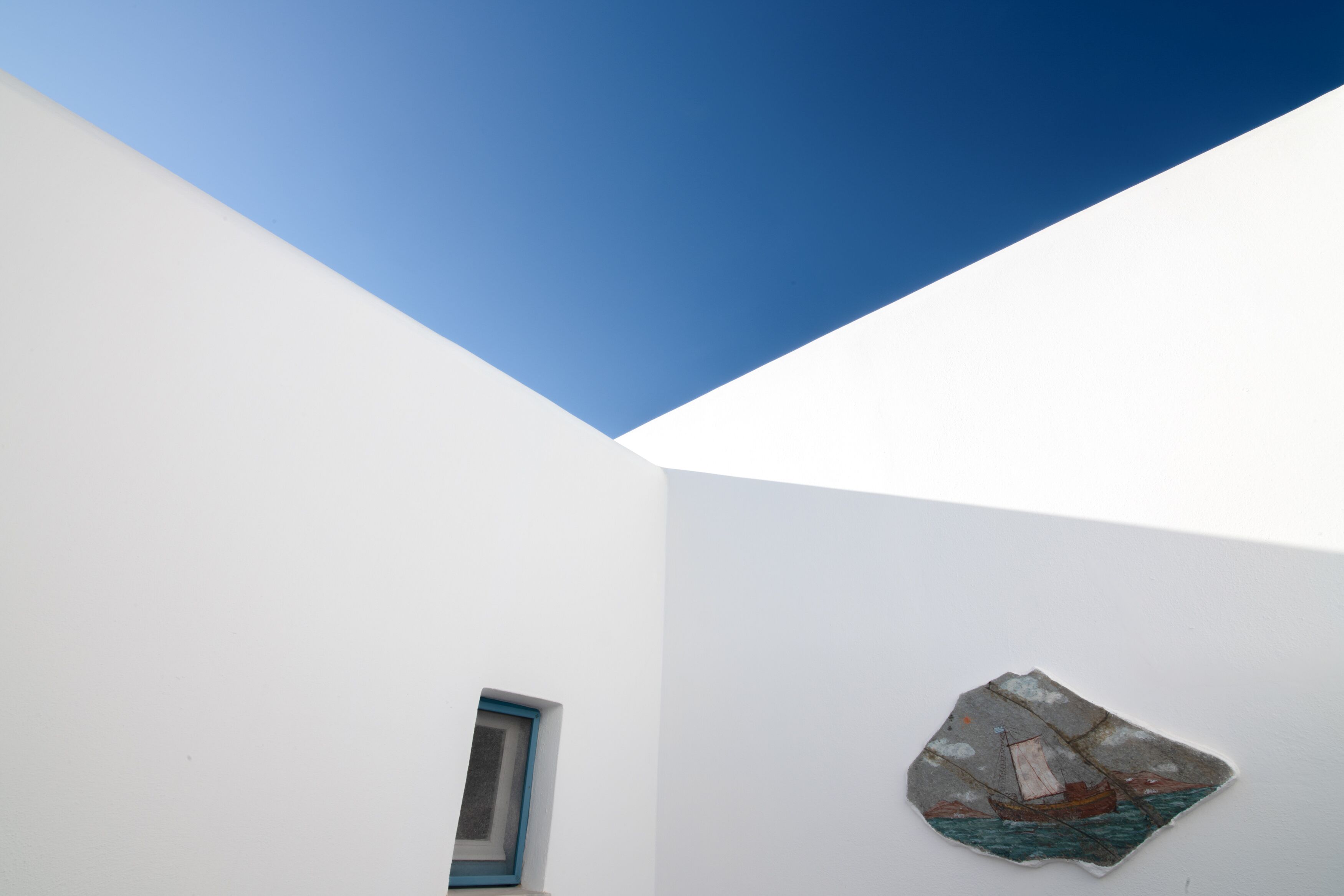 A room with a sloped ceiling, a small window, and a wall-mounted artwork depicting a sailboat.