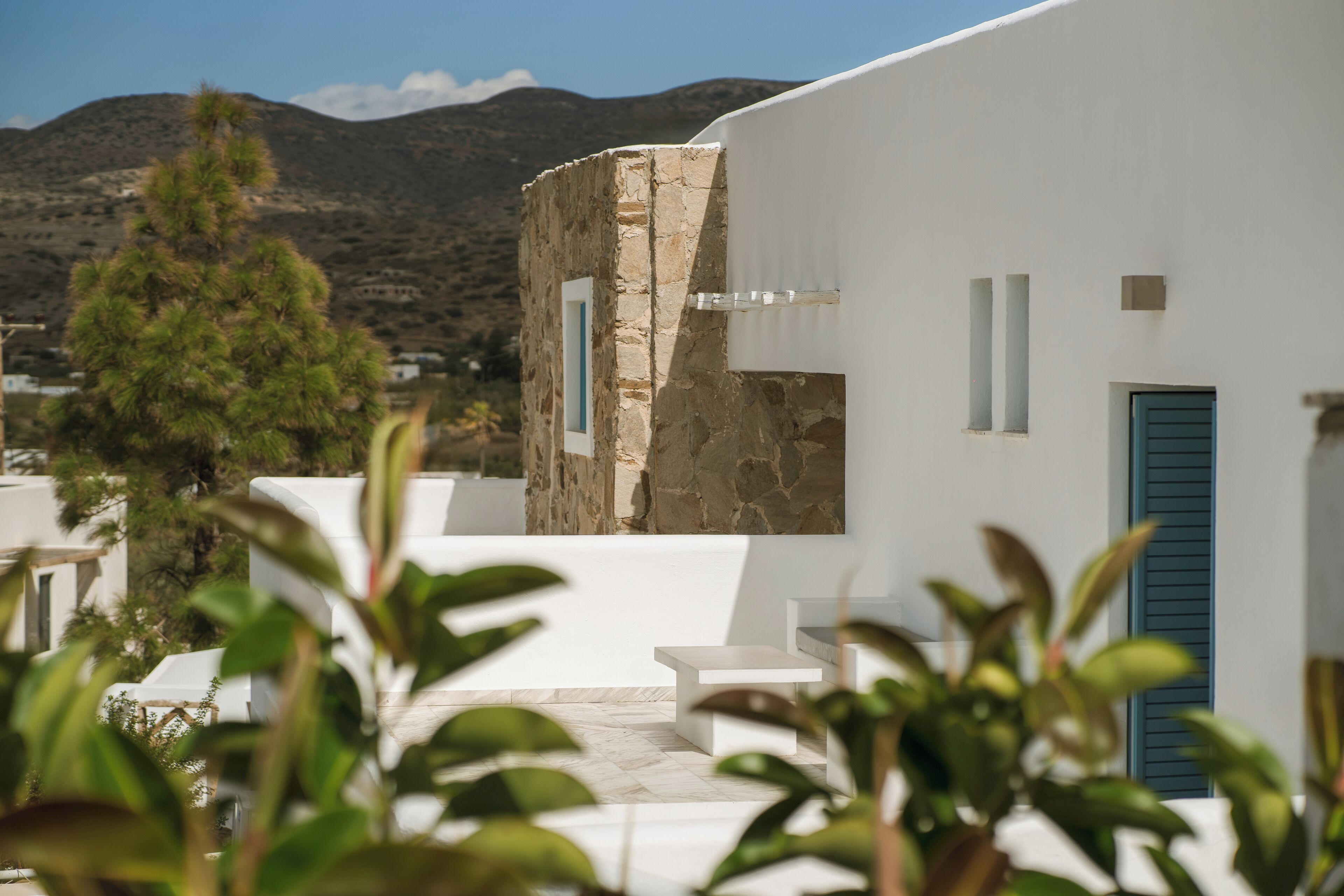 A white building with a stone facade, a blue door, and a view of a mountain.