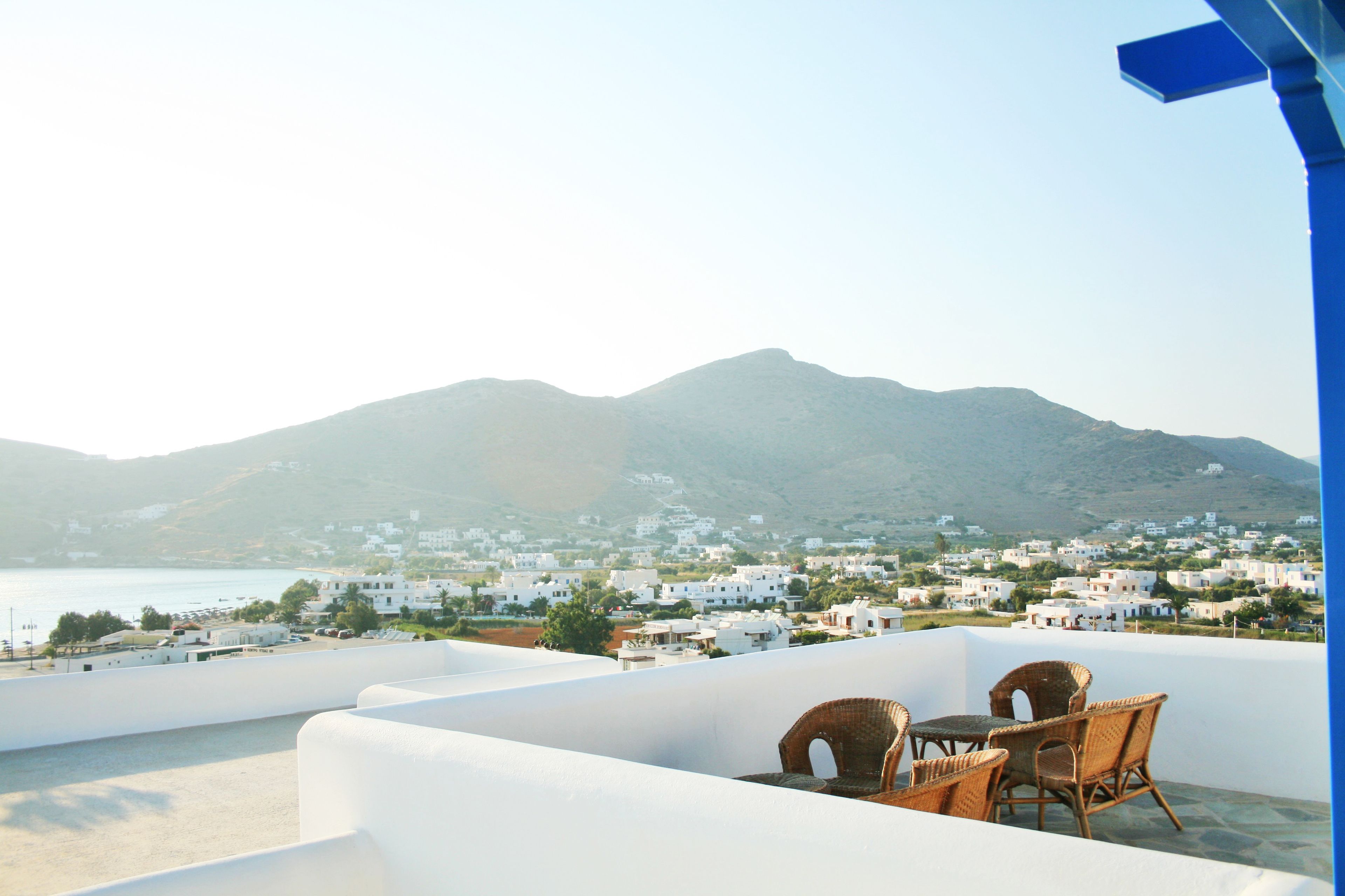 A terrace with wicker furniture overlooking a coastal town and mountains.