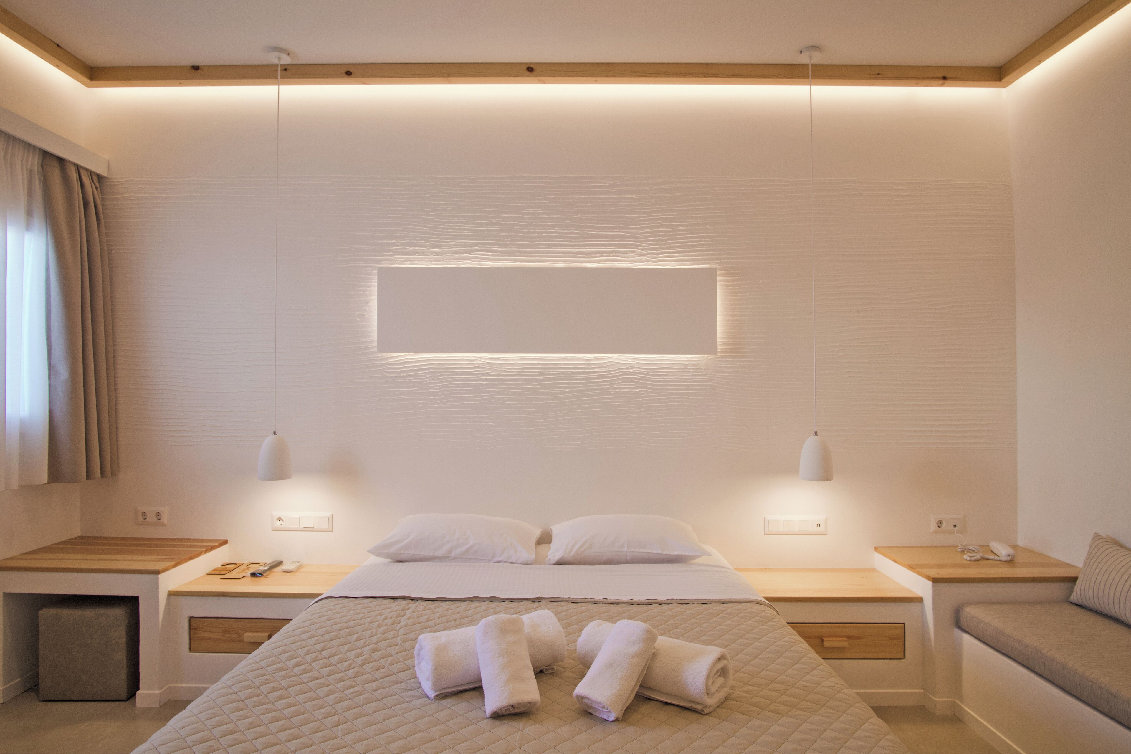 Quarto de hotel moderno com uma cama grande, mesas de cabeceira, abajures e uma TV de tela plana fixada na parede.