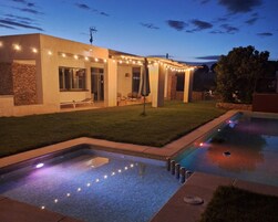 A modern outdoor pool area with a stone wall, lounge chairs, and string lights.