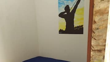 A single bed with a blue mattress in a room with a white wall and a mural of a person flying a kite.