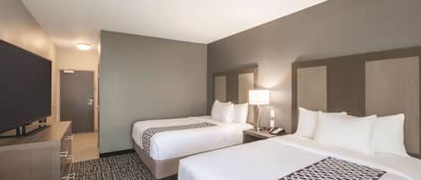 A hotel room with two beds, a TV, a desk, and a patterned carpet.